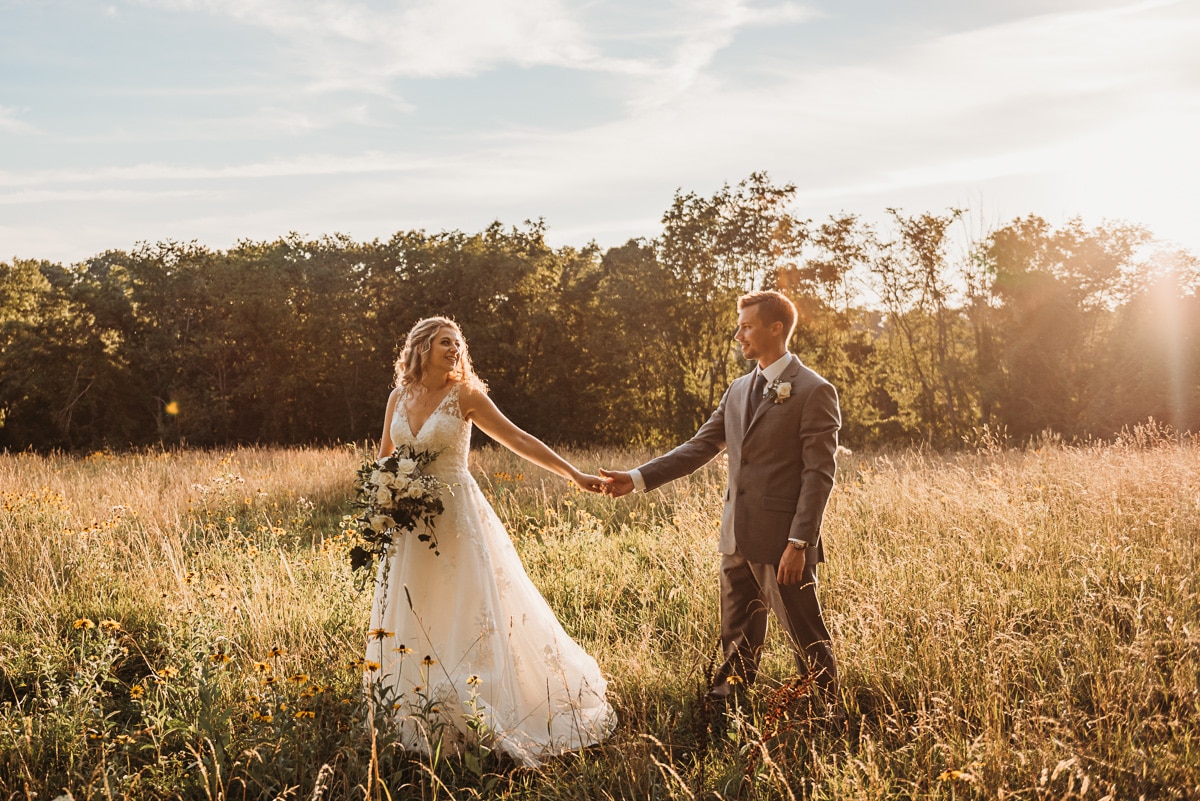 Just married couple walking through field at sunset